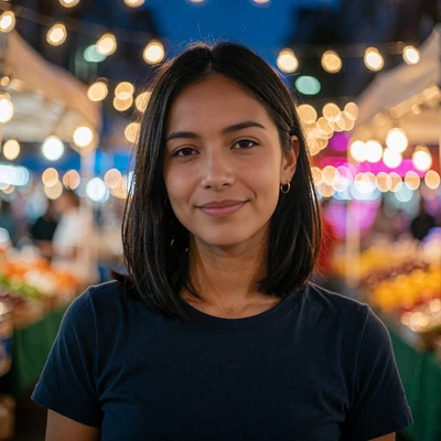 Woman in a navy t-shirt smiling at an open-air evening market, shown as a LatiMeets Latin dating member portrait